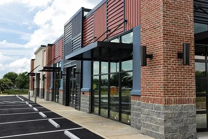 A modern commercial building with large windows, brick, and metal siding, situated in front of an empty parking lot, offers the perfect location for New Jersey Junk Removal Services.