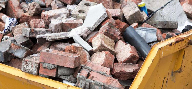 A yellow skip is filled with a variety of bricks, rubble, and construction debris.